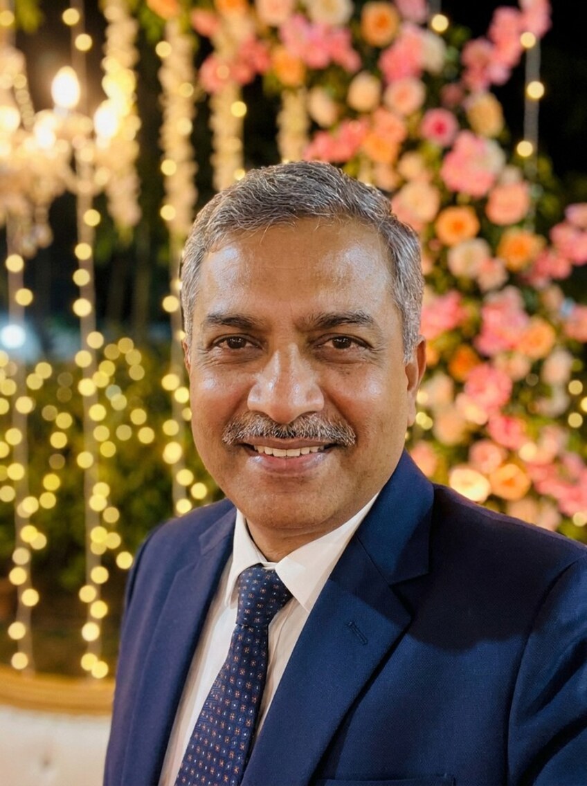 A smiling man in his late fifties in a navy suit, white shirt and patterned navy tie, photographed by the booth in front of a pink-and-peach floral wall hung with curtain-strings of fairy lights — the shot the booth just took