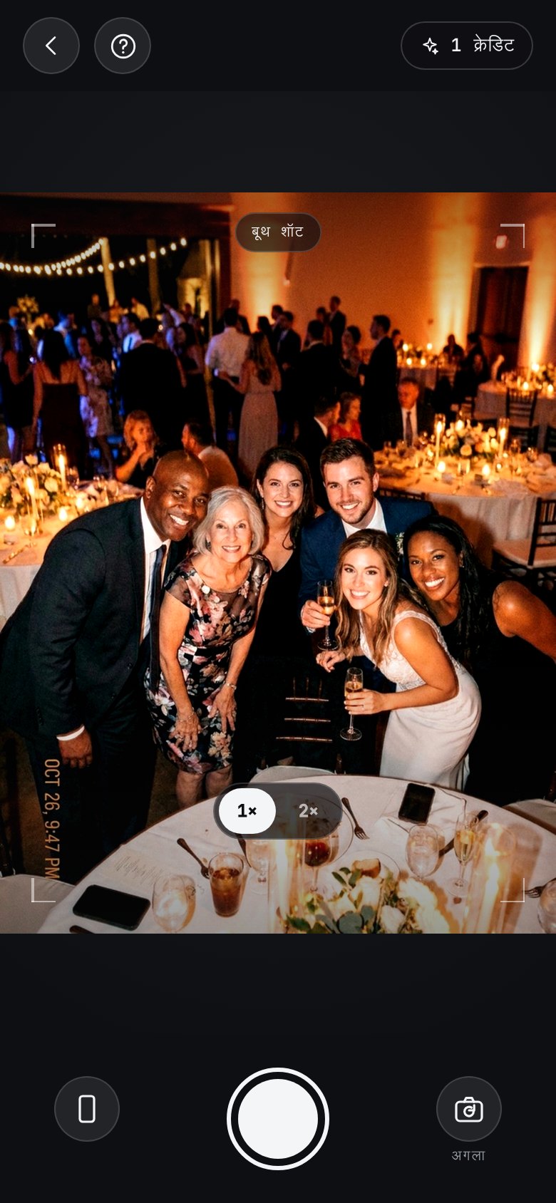The AI photobooth in the app: a camera of its own, open on a group of guests leaning in at a candlelit reception, with a “booth shot” badge across the viewfinder, a help button top-left and the booth credits left top-right