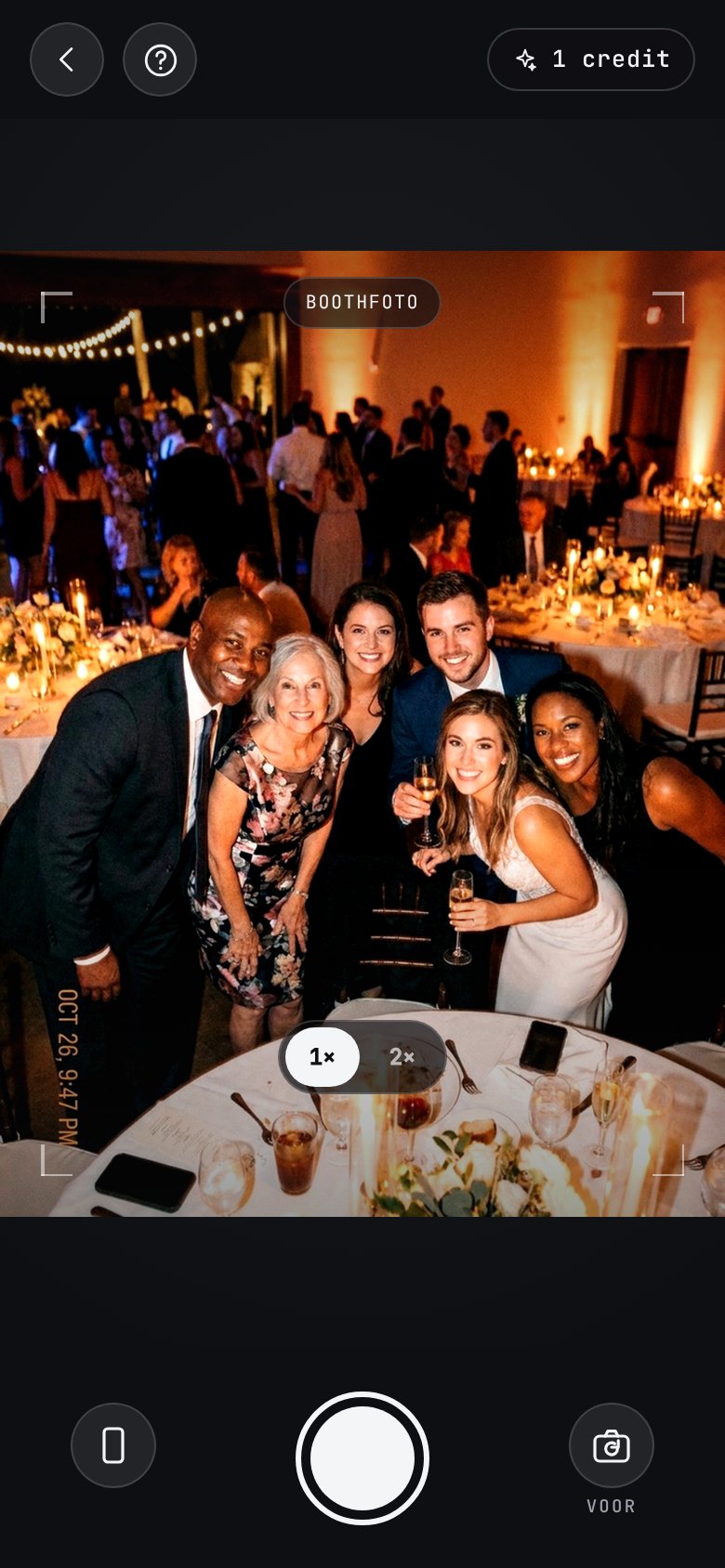 The AI photobooth in the app: a camera of its own, open on a group of guests leaning in at a candlelit reception, with a “booth shot” badge across the viewfinder, a help button top-left and the booth credits left top-right